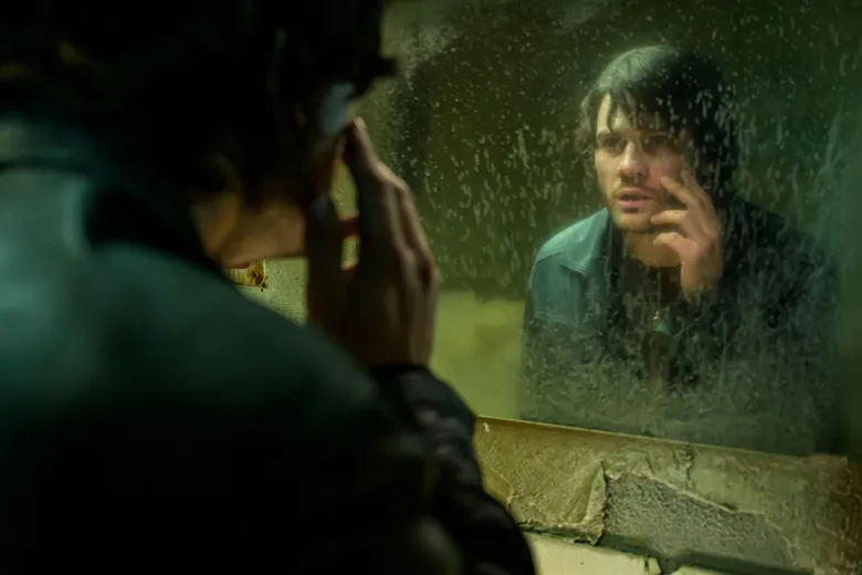 James se olha em um espelho sujo num banheiro imundo de beira de estrada